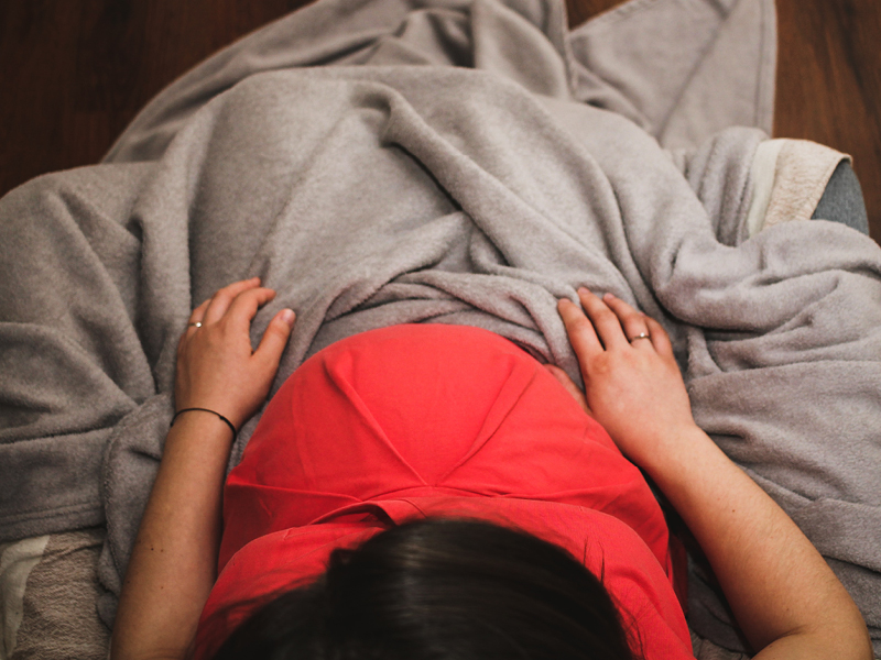 Overhead photo of a pregnant woman. Shows the top of her head, stomach, and a blanket covering her crossed legs in seated position